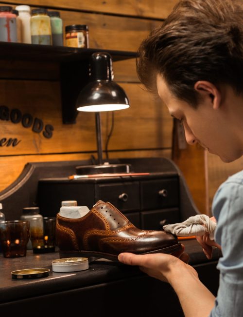 Picture of young concentrated shoemaker in workshop making shoes. Looking aside.